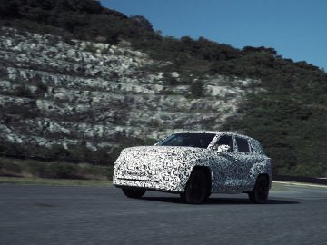 Een Lexus SUV met DIRECT4-technologie ondergaat wegtests op een snelweg langs een rotsachtige heuvel.