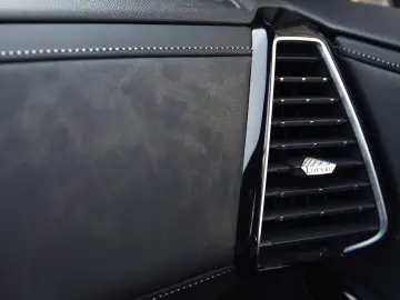 Close-up van de ventilatieopening van een DS 7 CROSSBACK-auto op een zwartleren dashboard met een klein label met de tekst 'lover.