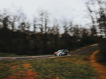 Een Peugeot 208 Rally 4 die te hard rijdt op een bochtige bosweg met bewegingsonscherpte-effect op de bomen.