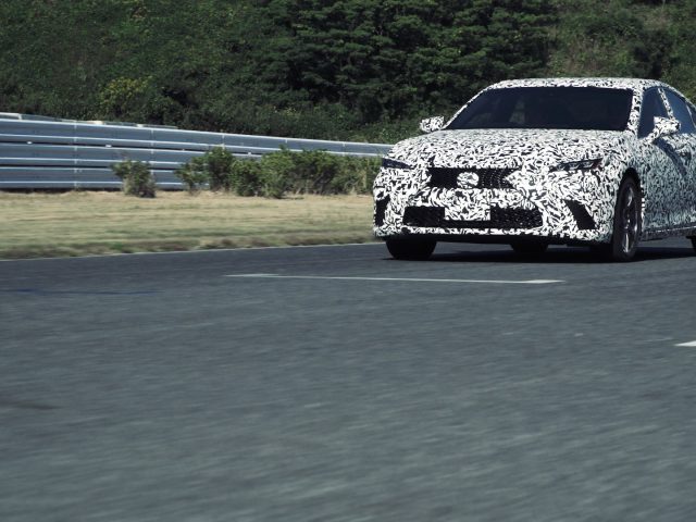Een Lexus DIRECT4-prototype, gecamoufleerd voor discretie, wordt getest op hoge snelheid op een snelweg met metalen barrières langs de weg.