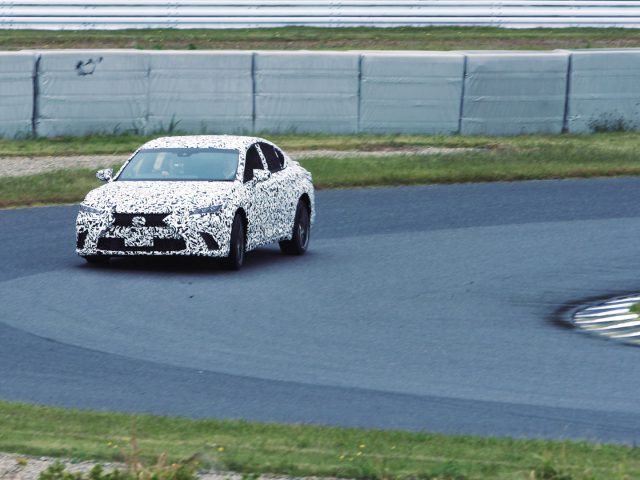Een Lexus met een camouflagepatroon die het DIRECT4-systeem test op een racecircuit en een bocht maakt met zichtbare bandensporen op het asfalt.