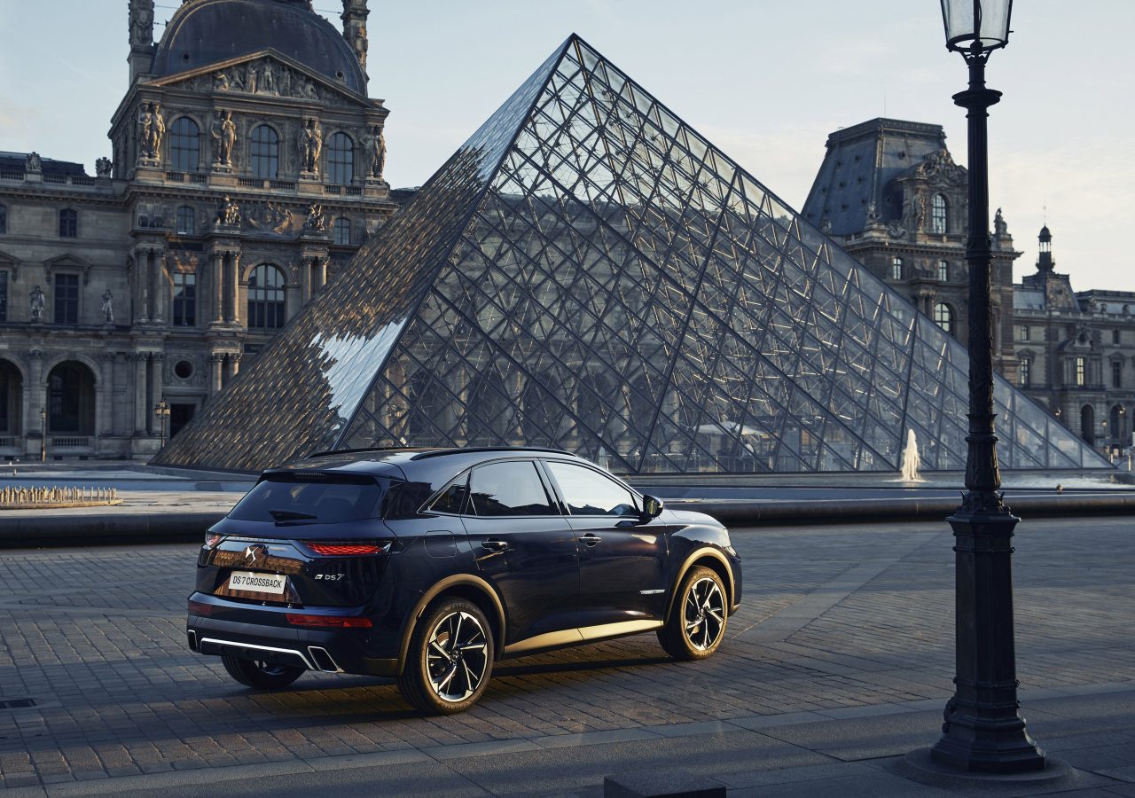 Een luxe SUV DS 7 CROSSBACK geparkeerd voor de piramide van het Louvre bij zonsondergang, met het historische gebouw van het Louvre Museum op de achtergrond.