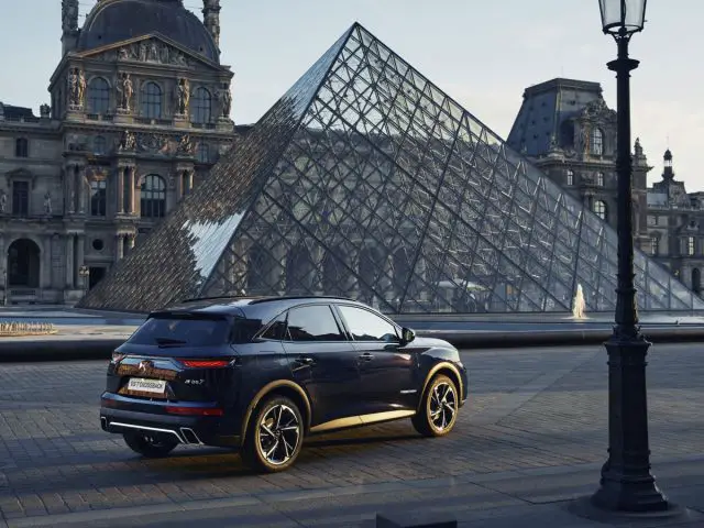 Een luxe SUV DS 7 CROSSBACK geparkeerd voor de piramide van het Louvre bij zonsondergang, met het historische gebouw van het Louvre Museum op de achtergrond.