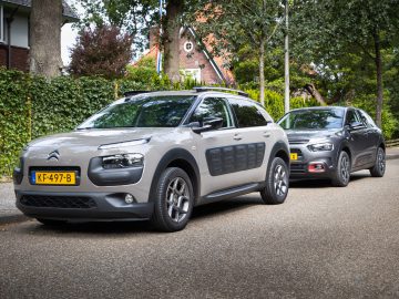 Twee moderne auto's geparkeerd in een lommerrijke woonstraat, met een grijze Citroën C4 Cactus op de voorgrond en daarachter een donkergrijze hatchback.