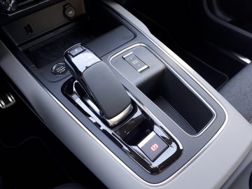 Auto-interieur van een C5 Aircross Hybrid met een automatische versnellingspook, bijbehorende bedieningselementen en een smartphone die op een draadloos oplaadstation rust.