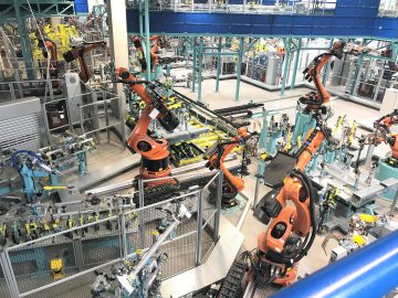 Hoge hoekmening van een drukke fabrieksvloer van INEOS Automotive met meerdere oranje robotarmen en apparatuur die producten assembleert.