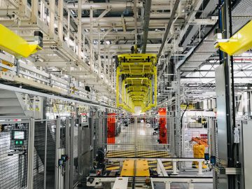 Een moderne geautomatiseerde productiefaciliteit gerund door INEOS Automotive, met robotarmen, transportbanden en veiligheidsbarrières in een goed verlichte ruimte.
