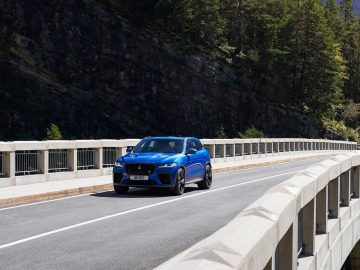 Een Jaguar F-Pace SVR die op een zonnige dag over een brug rijdt, omringd door hoge bergen.