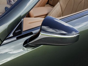 Close-up van de glanzende zijspiegel van een Lexus LC 500 Convertible met daarachter een luxueus beige lederen interieur.