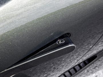 Close-up van een stoffige Lexus LC 500 Convertible met het logo aan de achterkant op de kofferbak met zichtbare stofdeeltjes en een lichte textuur.
