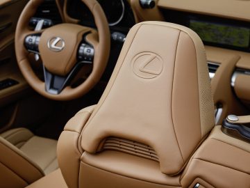 Binnenaanzicht van een Lexus LC 500 Convertible met een lichtbruine leren stoel met het Lexus-logo in reliëf op de hoofdsteun en een glimp van het dashboard.