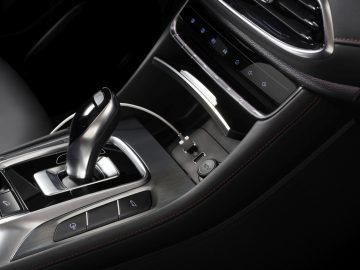 Binnenaanzicht van de MG EHS Plug-in Hybrid, met de versnellingspook, bedieningsknoppen en elegant zwart leer met stiksels.