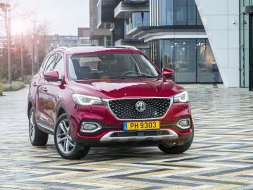 Rode MG EHS plug-in hybride SUV geparkeerd op een trottoir met patroon in een stedelijke omgeving bij daglicht.