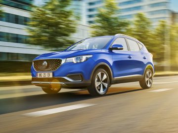 Een blauwe MG ZS SUV, gedekt door MG-garantie, rijdt op een zonovergoten weg omgeven door wazig groen, waarbij de beweging wordt benadrukt.