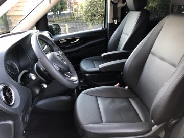 Binnenaanzicht van een Mercedes-Benz Vito met de bestuurdersstoel, de passagiersstoel voorin en het stuur, allemaal bekleed met zwart leer.