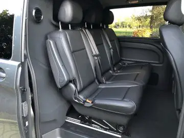 Binnenaanzicht van een Mercedes-Benz Vito met zwartleren achterstoelen met hoofdsteunen, veiligheidsgordels en een open deur aan de linkerkant.