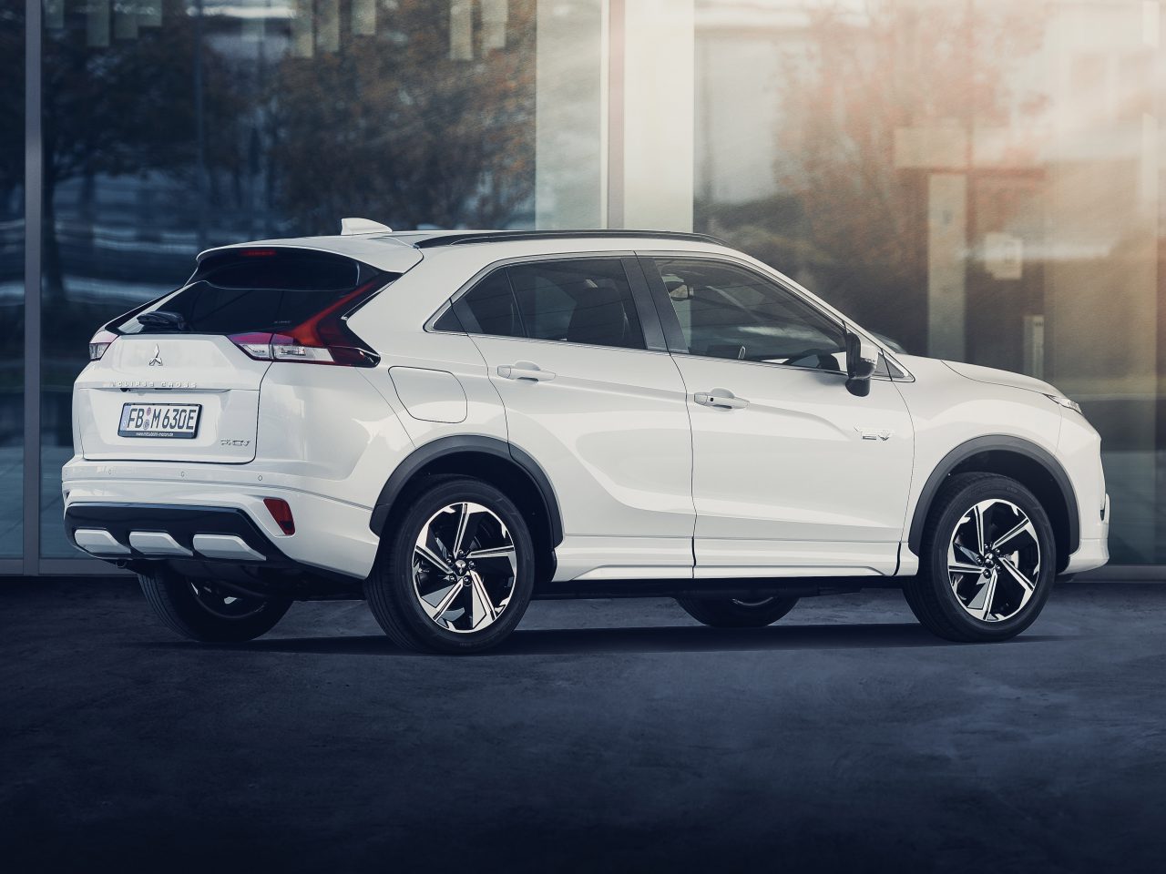 Witte Mitsubishi Eclipse Cross PHEV geparkeerd buiten een modern gebouw, met een strak ontwerp en gepolijste lichtmetalen velgen.