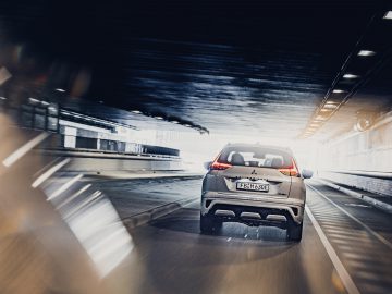 Een zilveren Mitsubishi Eclipse Cross PHEV hatchback die door een tunnel snelt, vage bewegingslijnen die hoge snelheid aangeven, focus op achterkant en kentekenplaat.