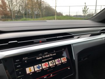 Uitzicht vanaf de bestuurdersstoel van een Volkswagen Arteon Shooting Brake met een dashboard met een digitaal beeldscherm afgestemd op een radiostation, omgeven door strakke, moderne designelementen.