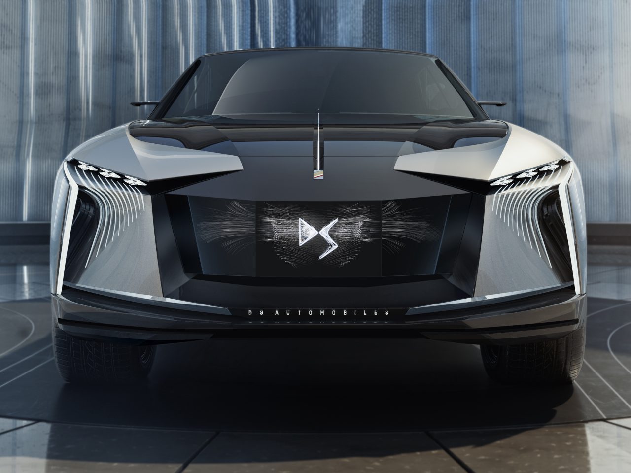 Een moderne elektrische auto DS 4 met een opvallende verlichte grille en scherpe hoeklijnen, tentoongesteld in een showroomsetting.