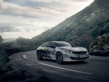Een gecamoufleerde Peugeot 508 PSE die onder een bewolkte hemel te hard rijdt op een bochtige bergweg.