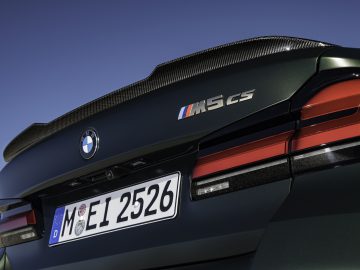 Close-up van het achteraanzicht van de donkergroene BMW M5 CS, met het embleem, de achterlichten en een Europees kenteken van de auto onder een helderblauwe lucht.