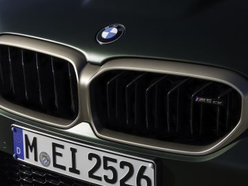 Close-up van de iconische grille en kentekenplaat van een BMW M5 CS, met het opvallende logo en de M5 CS-badge. De vlag van de Europese Unie en een 'D' voor Duitsland zijn duidelijk zichtbaar op het bord.