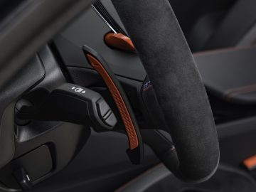 Close-up van het stuur van een auto met een schakelpeddel en richtingaanwijzerhendel. Het stuur, dat te vinden is in de BMW M5 CS, is bedekt met een gestructureerd materiaal en het interieur vertoont strakke, moderne designelementen.