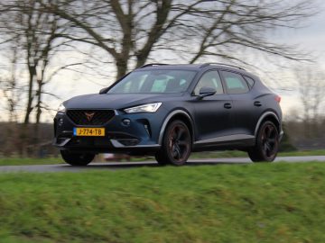Een donkergrijze Cupra Formentor in beweging op een landweg, met bomen op de achtergrond en een bewolkte lucht.