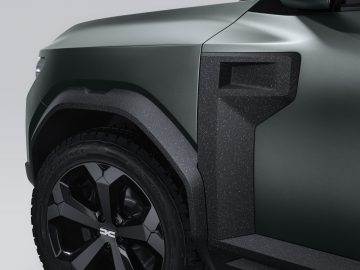 Close-up van een donkergrijze Dacia Bigster Concept SUV, waarbij de nadruk ligt op het voorwiel en het spatbord met een matte afwerking.