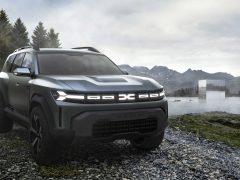 Een Dacia Bigster Concept SUV staat geparkeerd op een rotsachtig pad naast een mistig meer, met bergen en bomen op de achtergrond onder een bewolkte hemel.