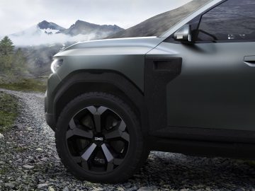 Close-up van de linker voorband van de Dacia Bigster Concept op een onverharde weg met mistige bergen op de achtergrond.