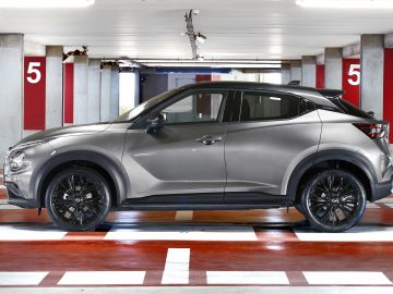 Een zilveren Nissan Juke geparkeerd in een overdekte parkeergarage, schuin tegenover een parkeerplaats, met rode en witte kolommen gemarkeerd met het cijfer 5 op de achtergrond.