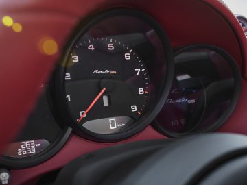 Close-up van het dashboard van een Porsche Boxster met de snelheidsmeter en toerenteller met de nadruk op de details en het rode interieur van de auto.