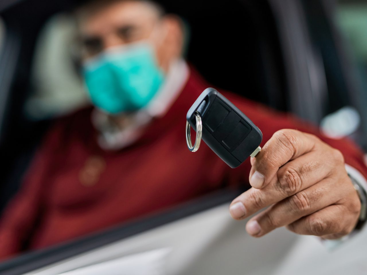 Persoon met gezichtsmasker die in een auto zit en een autosleutel aanbiedt voor een proefritauto.