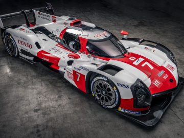 Hoge hoekmening van een witte en rode Toyota GR010 HYBRID-raceauto met sponsorlogo's, geparkeerd in een slecht verlichte garage.