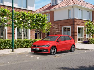 Rode Volkswagen Polo R-Line Edition geparkeerd in een zonnige straat in een woonwijk met moderne huizen en groene bomen.
