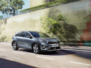 Een zilveren Kia Niro rijdt door een zonnige straat, waarbij het strakke ontwerp wordt onderstreept door de onscherpe achtergrond en de beweging ervan wordt benadrukt.