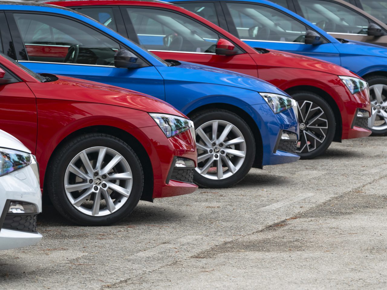 Een rij nieuwe auto's in de kleuren rood, blauw en wit, diagonaal geparkeerd op een parkeerplaats, met de nadruk op hun glanzende lichtmetalen velgen en strakke ontwerpen, klaar om aan de verkoopprognose voor personenauto's te voldoen.