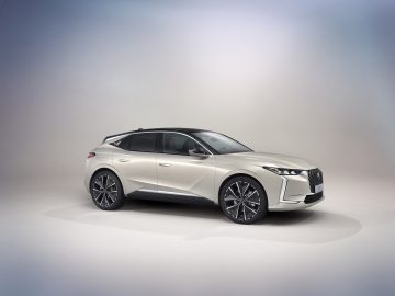 Tegen een neutrale achtergrond wordt een zilveren DS 4-luxeauto met strak design en donkergetinte ruiten getoond. Hij beschikt over opvallende wielen en een verfijnde grille aan de voorkant.