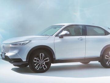 Een zilveren Honda HR-V wordt weergegeven tegen een lichtblauwe, studio-achtige achtergrond met zachte verlichting. Het profiel van het voertuig wordt weergegeven vanuit een hoek van de voorzijde.