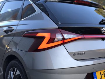 Close-up van de achterkant van een grijze Hyundai i20-auto met het achterlicht, het Hyundai-logo en een deel van een Europese kentekenplaat.