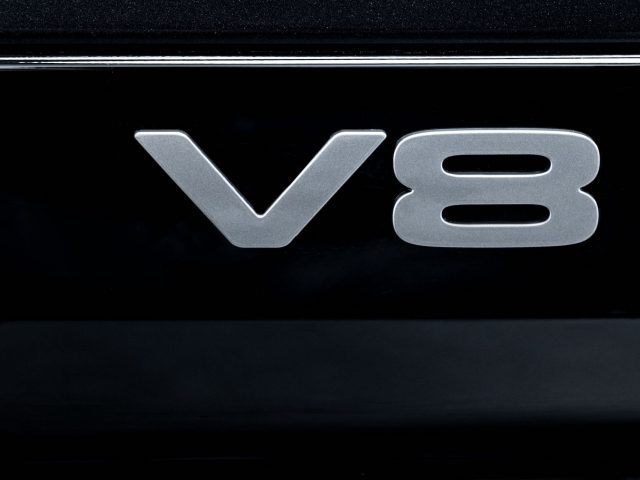 Close-up van een "V8"-embleem op een zwarte Land Rover Defender V8, wat de aanwezigheid van een krachtige V8-motor aangeeft.