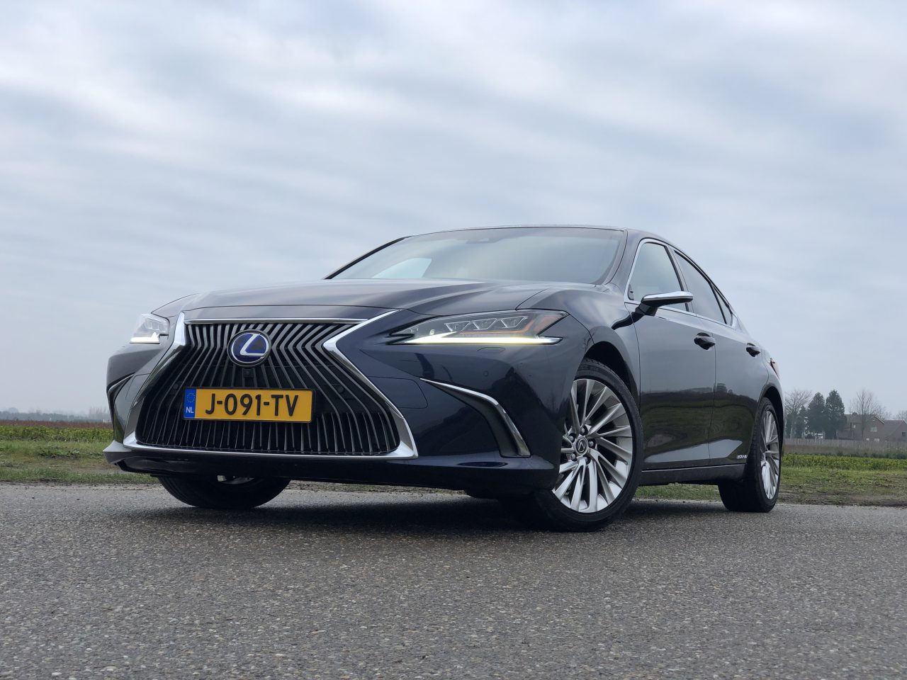 Een zwarte Lexus ES 300h geparkeerd op een weg, met een schuin vooraanzicht dat de opvallende grille en strakke koplampen laat zien, onder een bewolkte hemel.