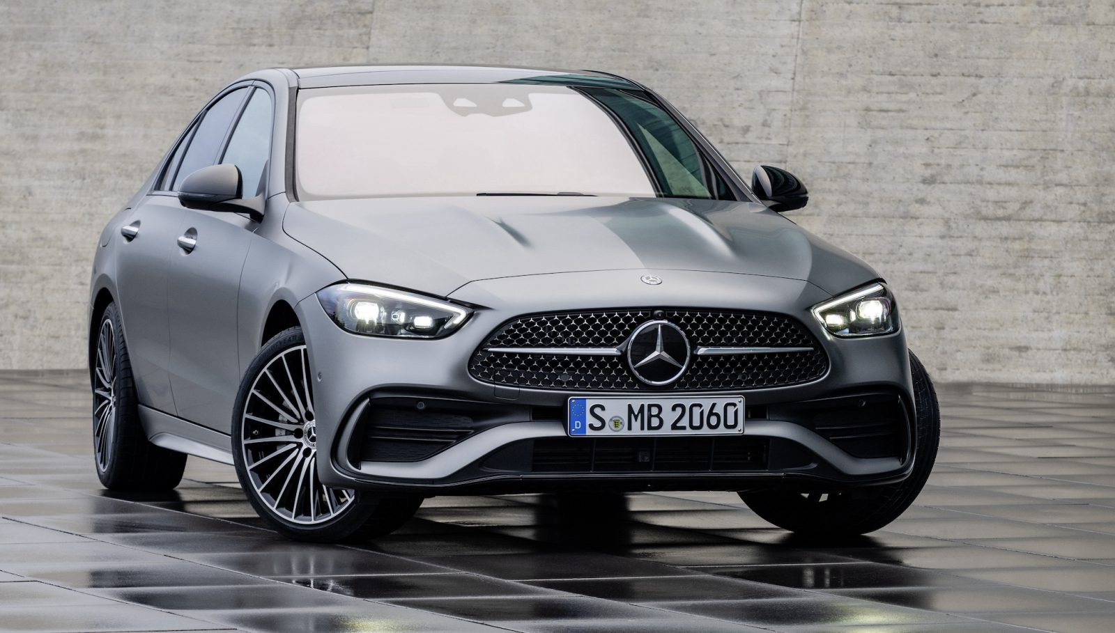 Een strakke grijze Mercedes-Benz C-Klasse sedan geparkeerd op een nat betegeld oppervlak tegen een betonnen muur.