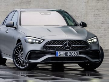 Een strakke grijze Mercedes-Benz C-Klasse sedan geparkeerd op een nat betegeld oppervlak tegen een betonnen muur.