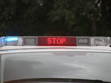 De bovenste lichtbalk van de politieauto met een rood 'STOP'-bericht en blauwe lichten aan weerszijden tegen een onscherpe achtergrond, wat de urgentie van de handhaving van de Verkeersboetes 2020 benadrukt.