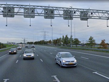 Een snelweg met meerdere rijstroken, waarbij meerdere auto's in beide richtingen rijden. Erboven bevindt zich een metalen portaal uitgerust met Trajectcontrole-camera's en elektronische apparatuur. De lucht is bewolkt.