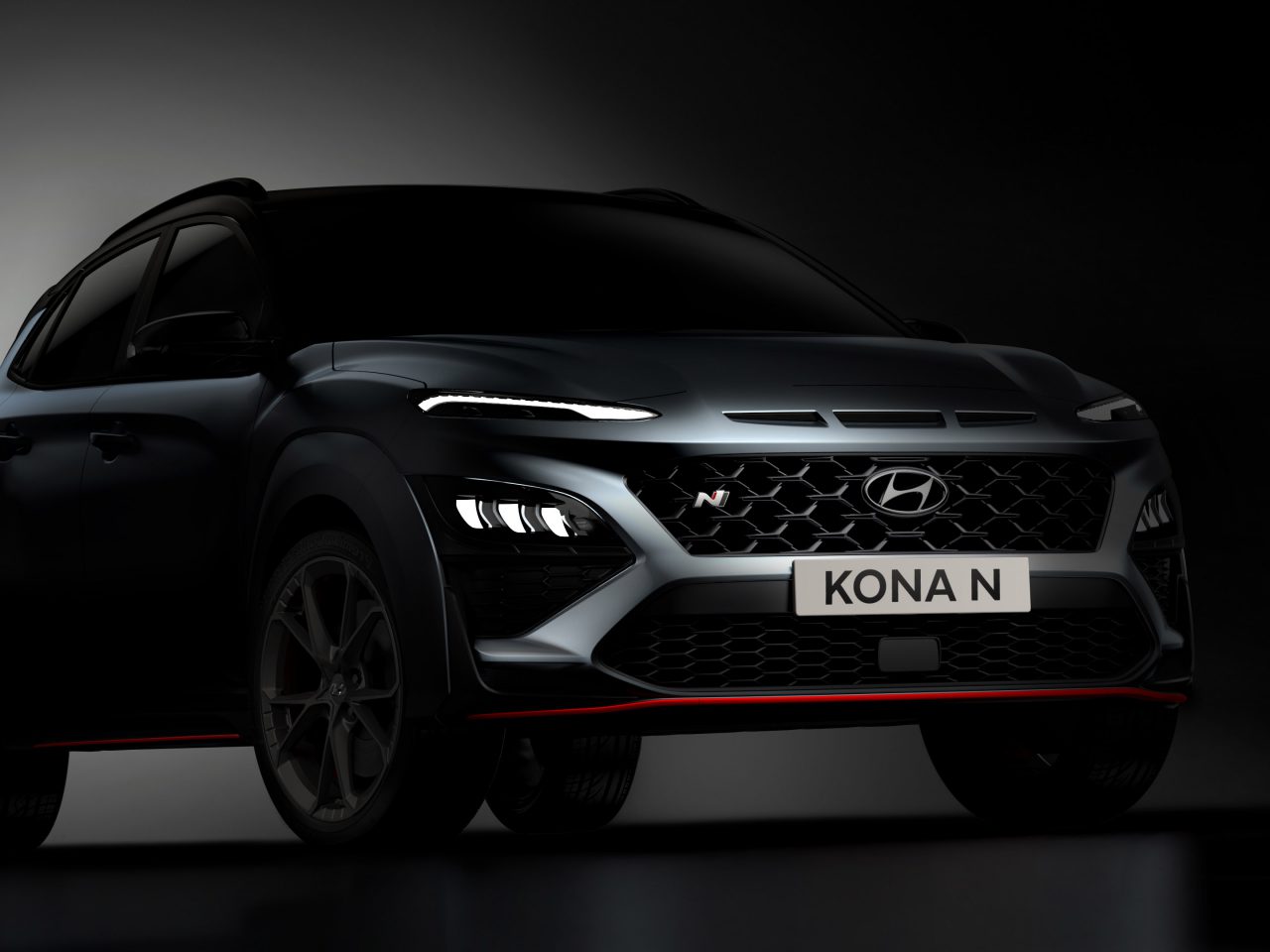 Een donker beeld van een Hyundai Kona N-auto met verlichte LED-koplampen en een grille aan de voorkant. Op het kenteken staat ‘KONA N’, wat het gedurfde ontwerp van de prestatievariant van de Hyundai Kona benadrukt.