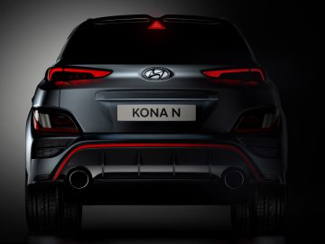 Achteraanzicht van een donkergekleurde Hyundai Kona N SUV met verlichte rode achterlichten, een zichtbaar Hyundai-logo en dubbele uitlaten, tegen een donkere achtergrond.